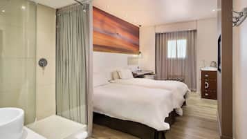 A hotel room with a glass-enclosed shower, two beds with white bedding, a painting on the wall, a desk with a lamp, and a wardrobe.