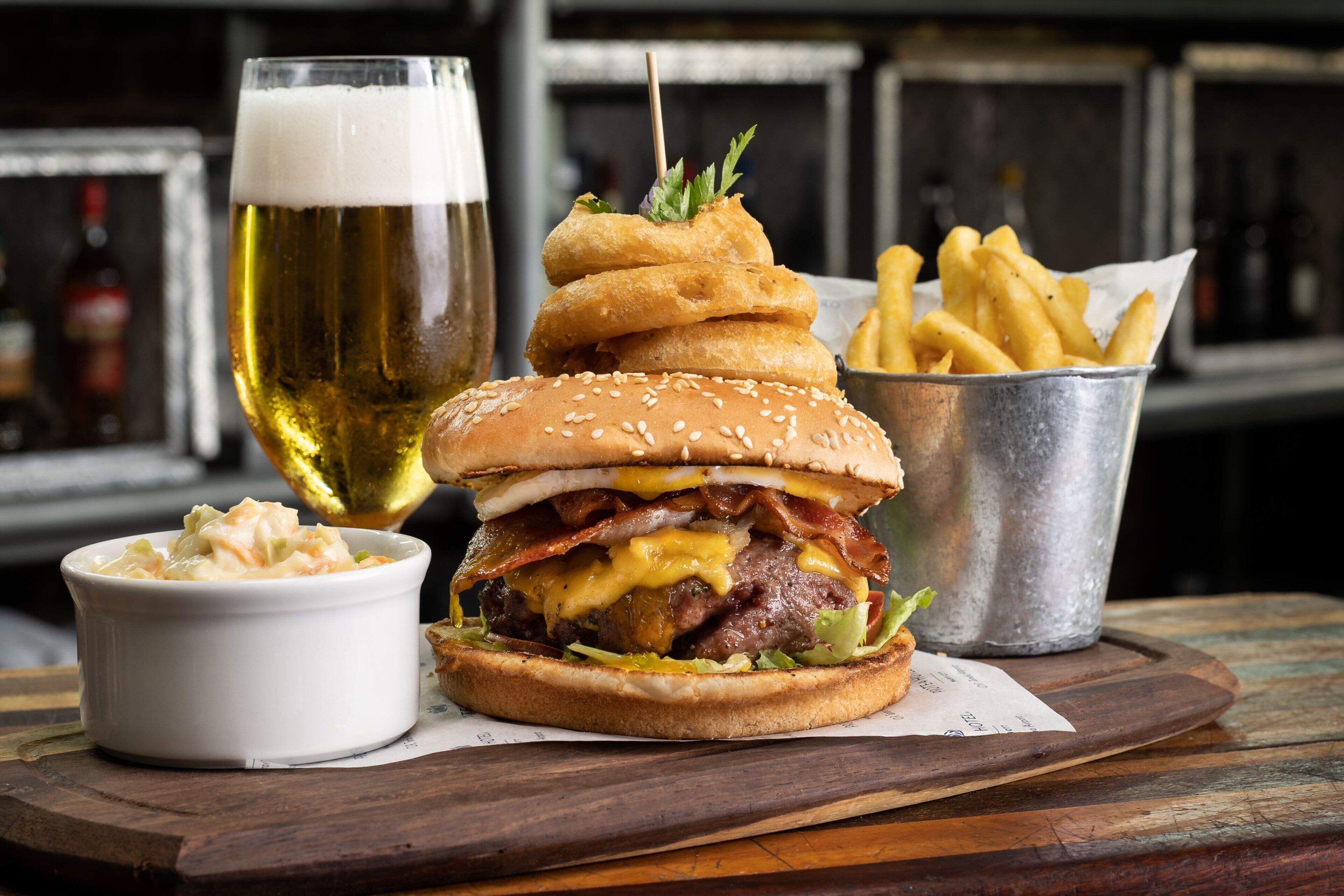 A burger with fries and a beer on a wooden table.