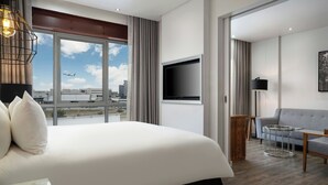 A modern hotel room with a large bed, a flat-screen TV, a sofa, and a view of the cityscape. - Protea Hotel by Marriott O.R. Tambo Airport (Kempton Park)