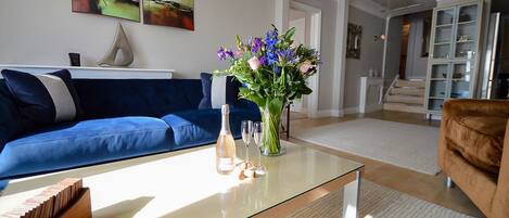 A living room with a blue sofa, a glass coffee table, and a vase of flowers.