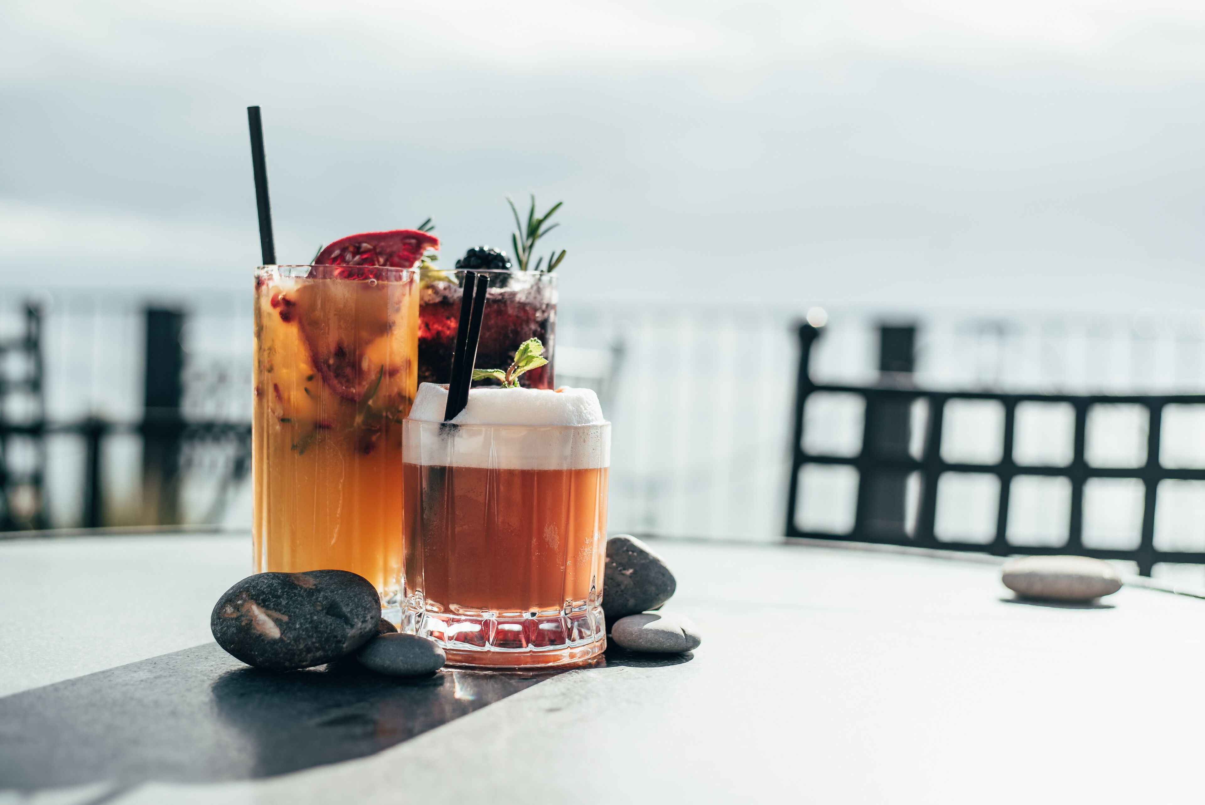 Two glasses of iced beverages on a table with rocks, set against a blurred outdoor background.