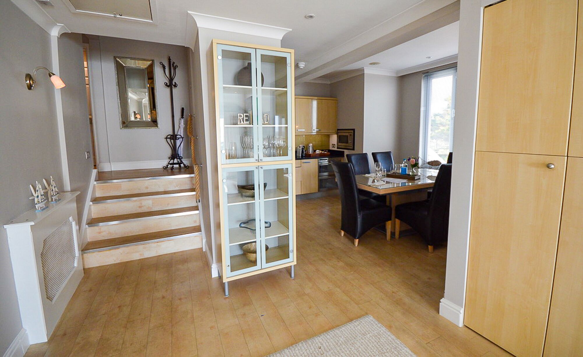 A spacious living area with a staircase, a dining table with chairs, and a kitchen in the background.