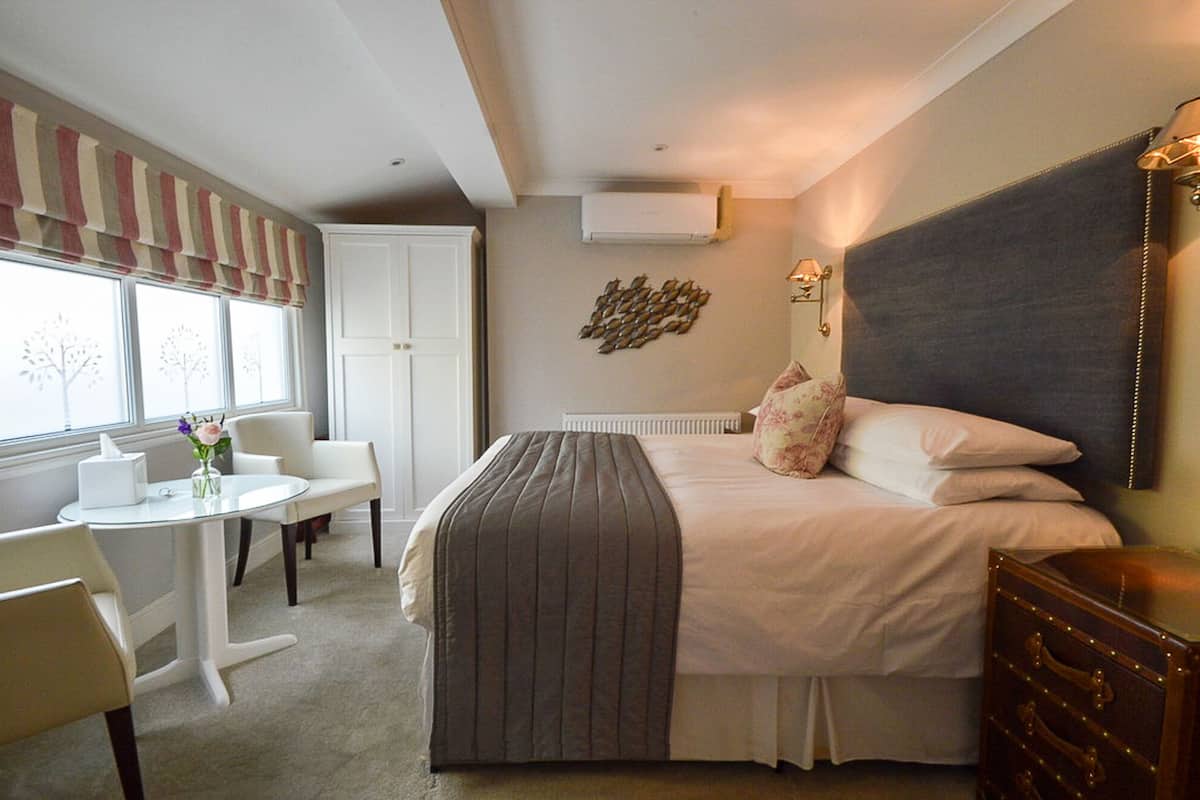 A hotel room with a bed, bedside table, chair, and a small table with a vase of flowers.