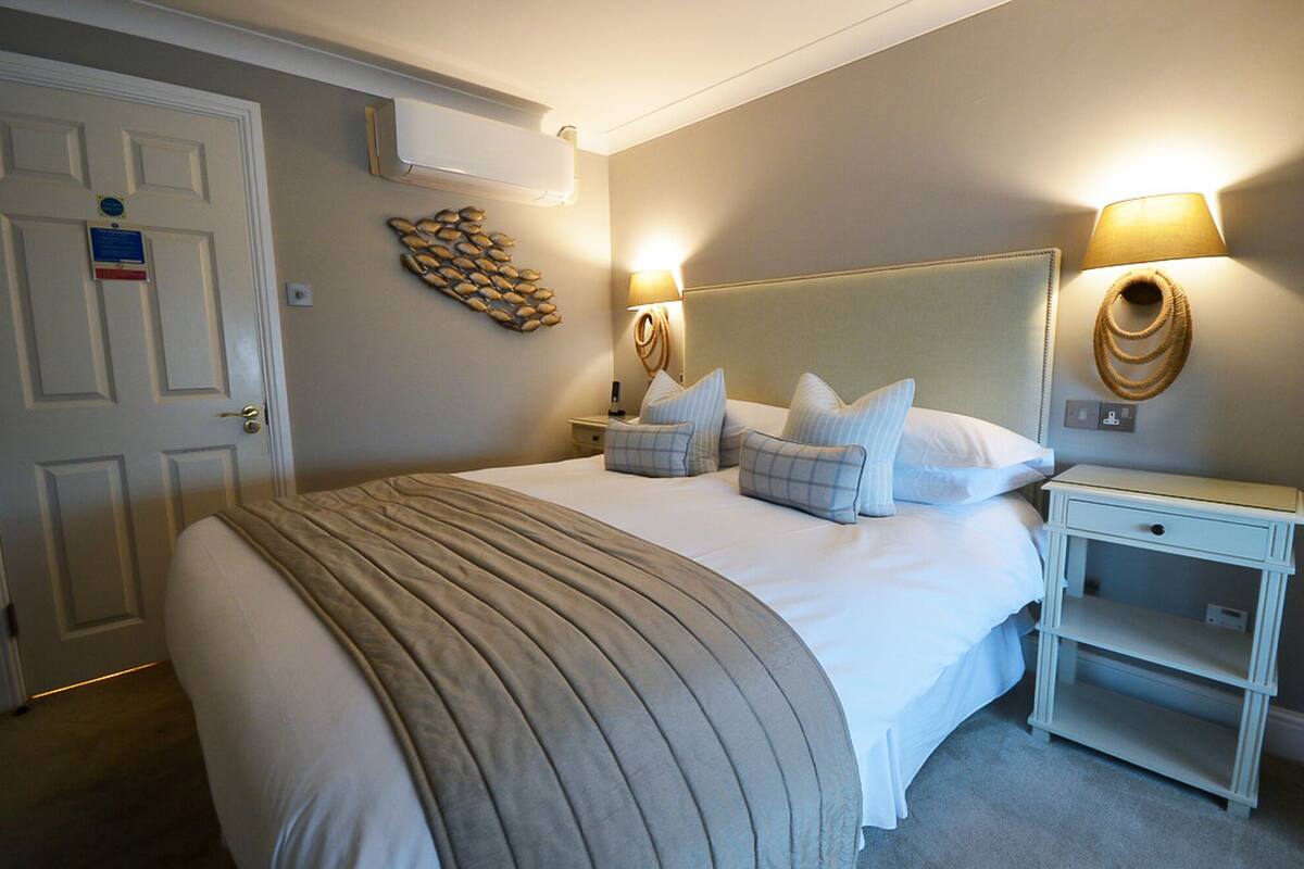 A neatly arranged bedroom with a large bed, bedside lamps, a bedside table, and a wall-mounted air conditioner.
