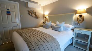 A neatly arranged bedroom with a large bed, bedside lamps, a bedside table, and a wall-mounted air conditioner.