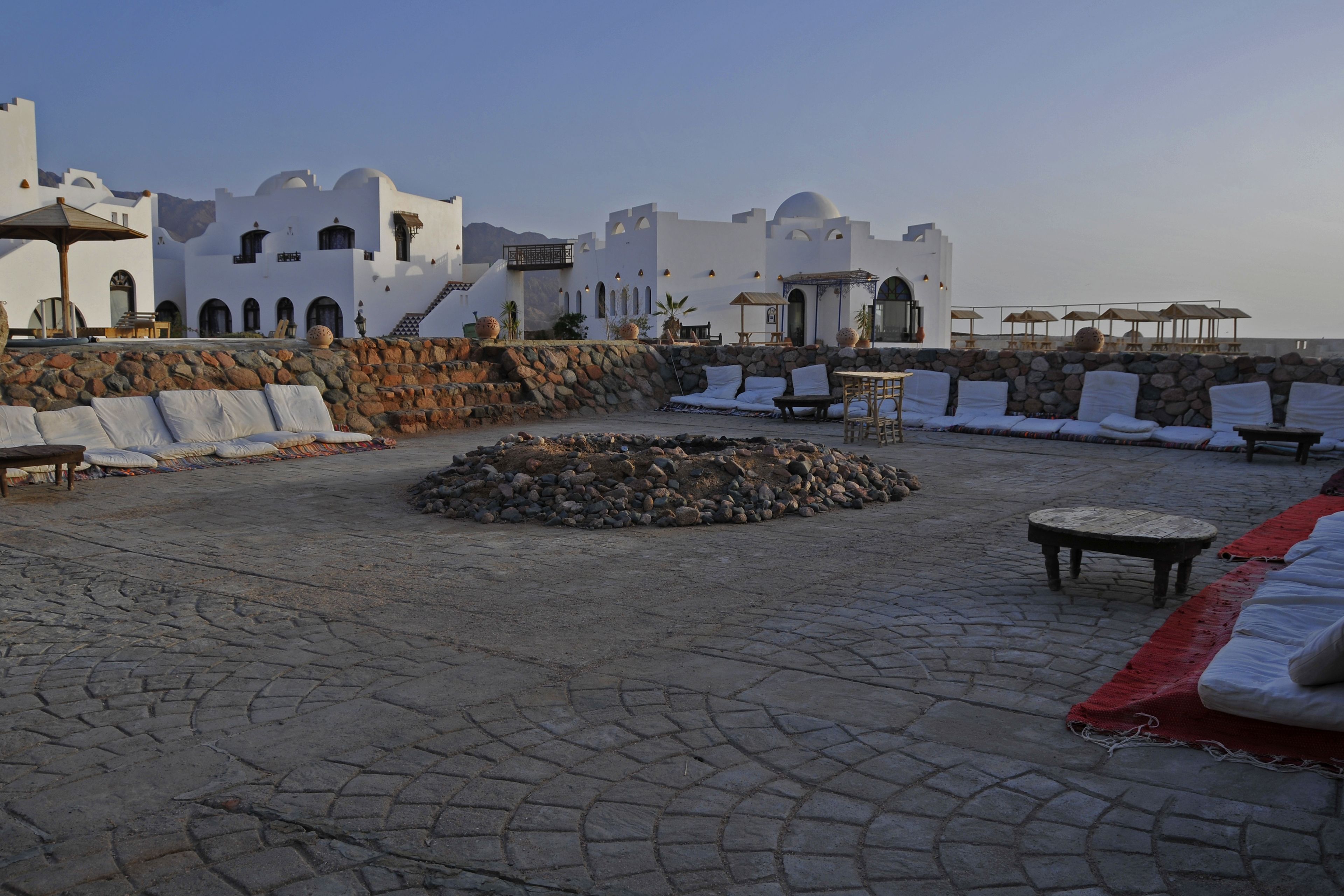 A rooftop terrace with stone flooring, white lounge chairs, and a stone fire pit.