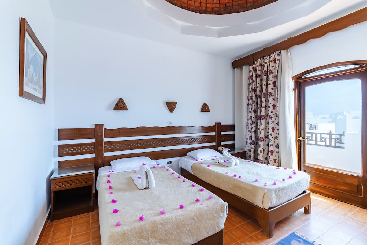 A hotel room with two beds, a wooden headboard, a framed picture on the wall, and a view through a window.