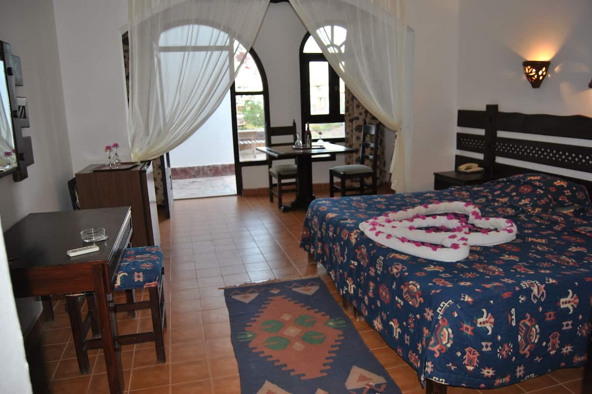 A bedroom with a bed, a desk, a chair, and a window with curtains.