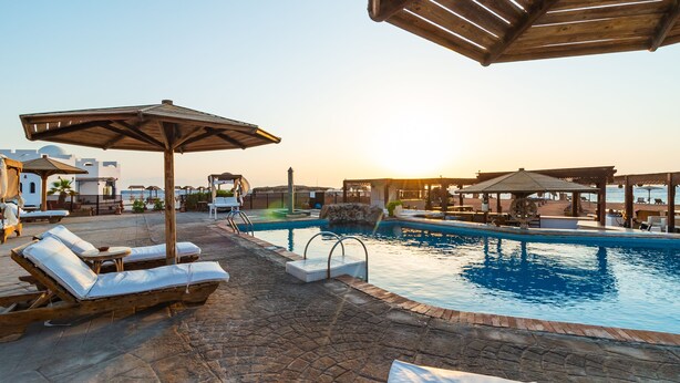 A pool area with lounge chairs and umbrellas, a stone-tiled floor, and a view of the sea. - Daniela Village Dahab (Dahab)