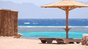A beach with a wooden umbrella and a rustic hut, overlooking the ocean. - Daniela Village Dahab (Dahab)