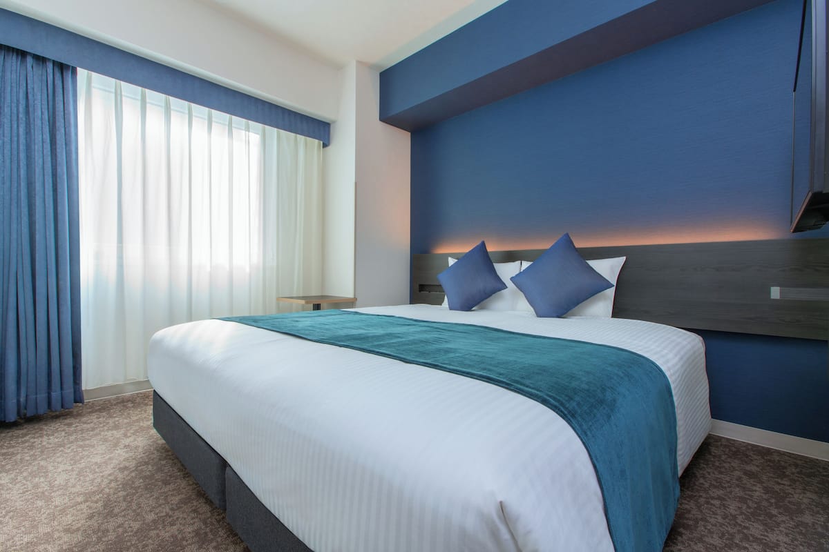 Una habitación de hotel con una cama grande, una mesita de noche y un ventanal con cortinas.