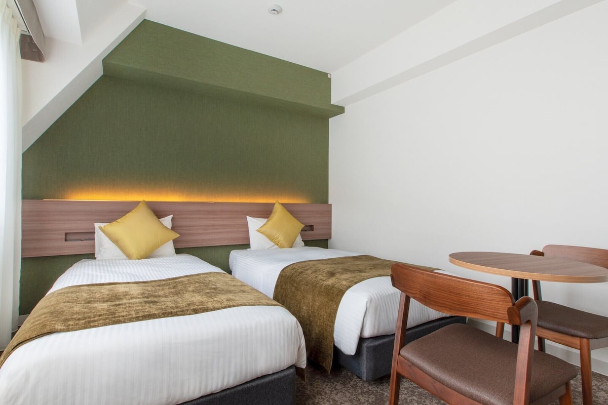 Habitación de hotel con dos camas, una mesita redonda y una silla.