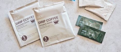 Two bags of drip coffee and two packets of creaming powder on a textured surface.