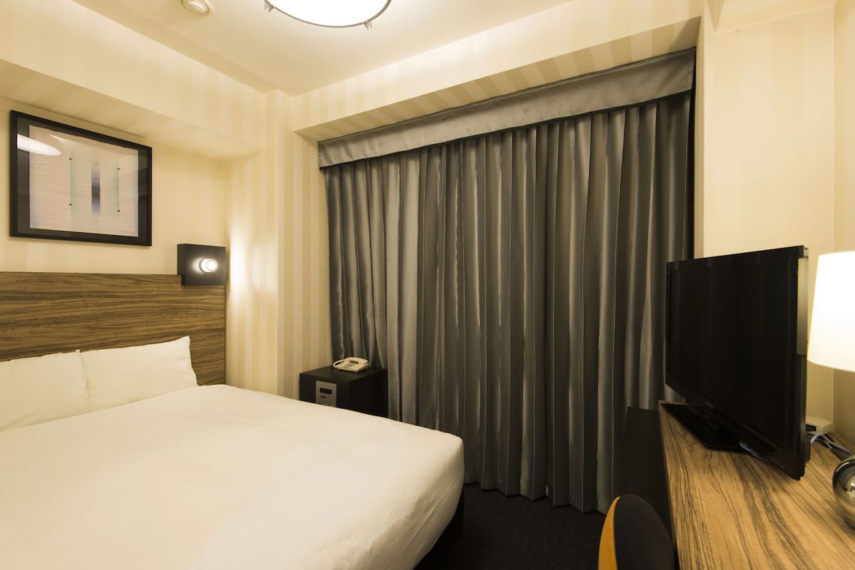 A hotel room with a bed, a desk with a lamp, a television, and a curtain.