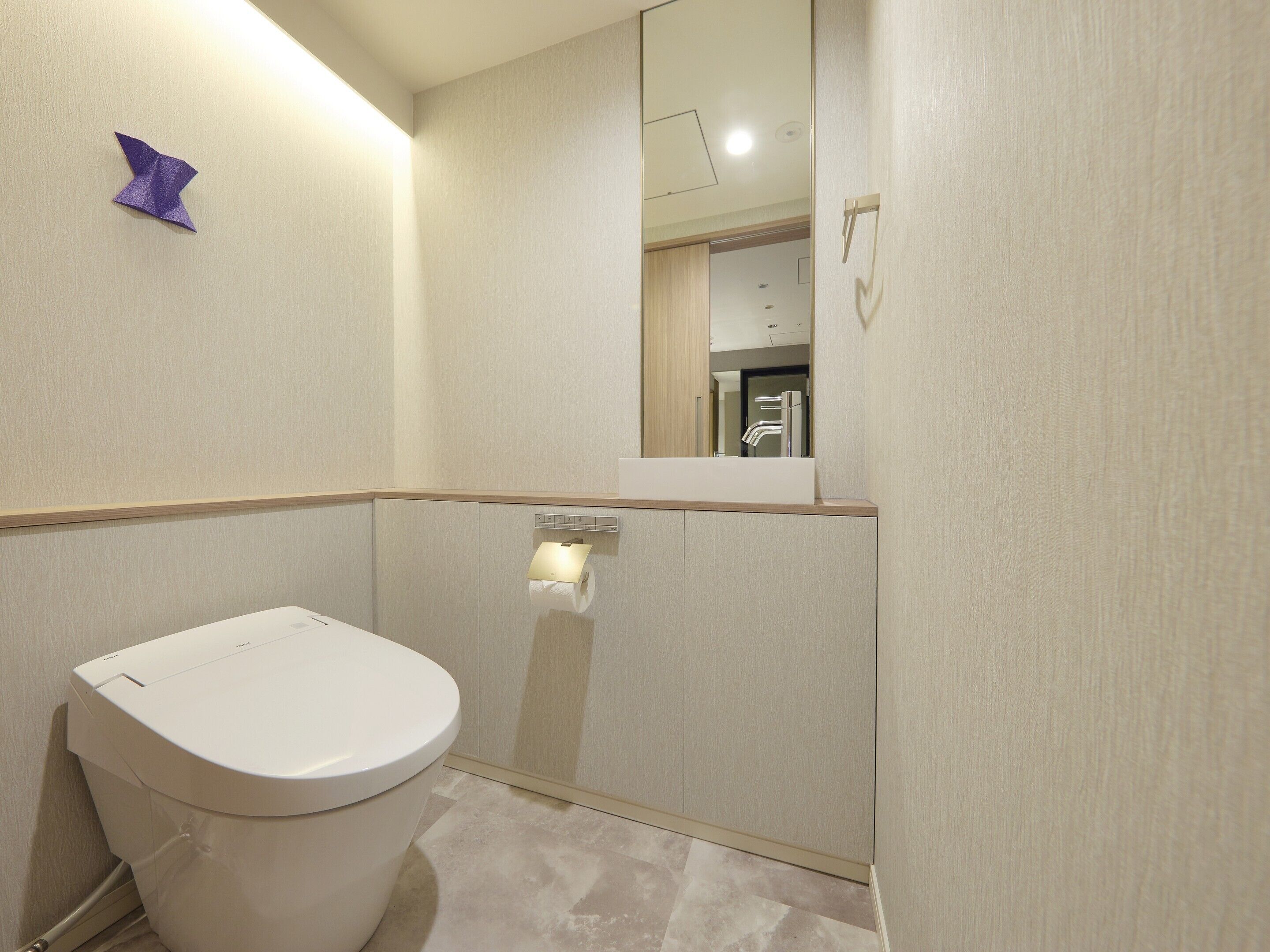 A modern bathroom with a toilet, a mirror, and a towel dispenser.
