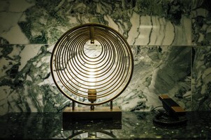 A circular metallic object with concentric rings on a reflective surface, possibly a decorative piece or a functional item, against a marble background.