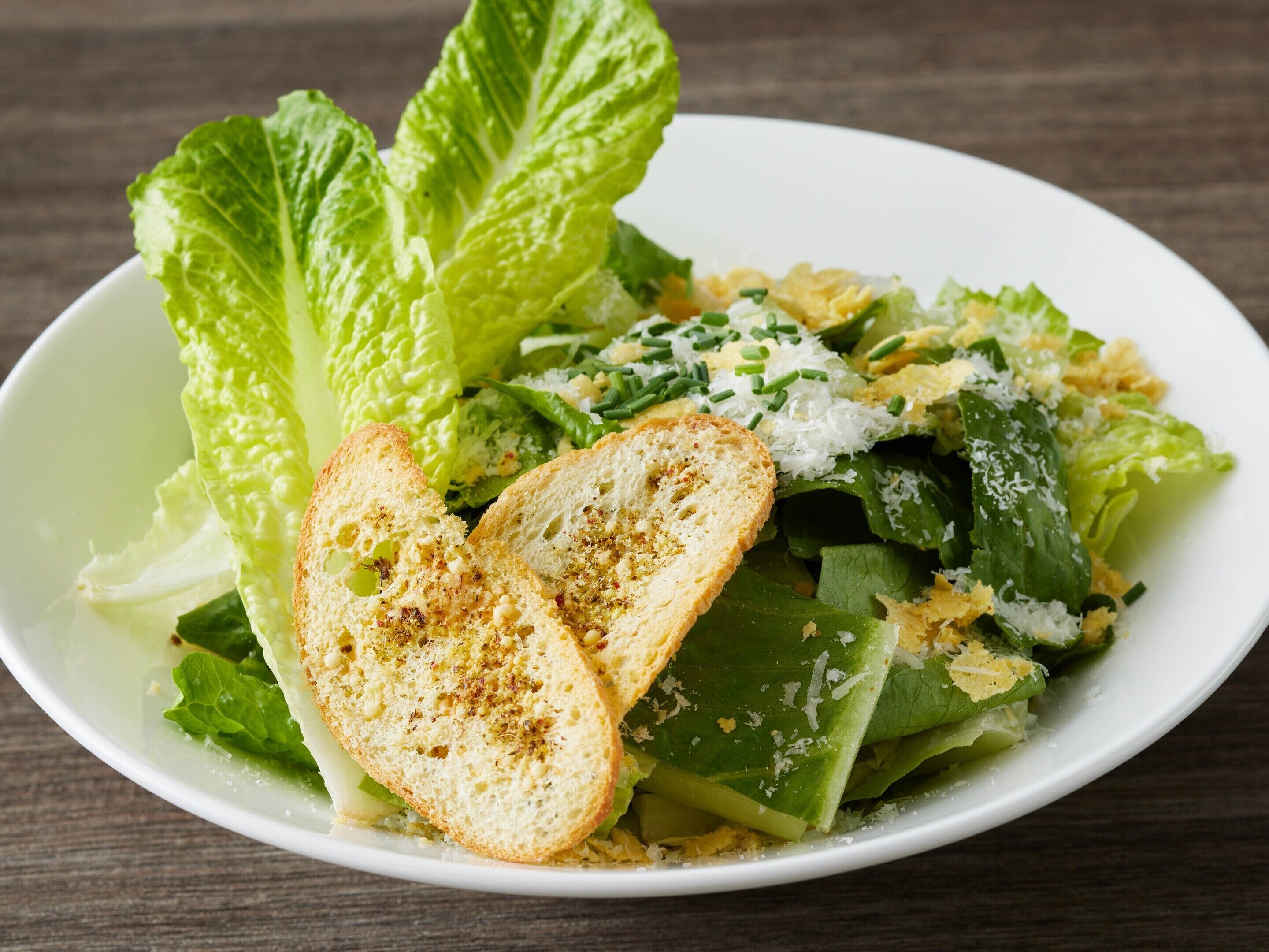 A plate of green salad with croutons and grated cheese.