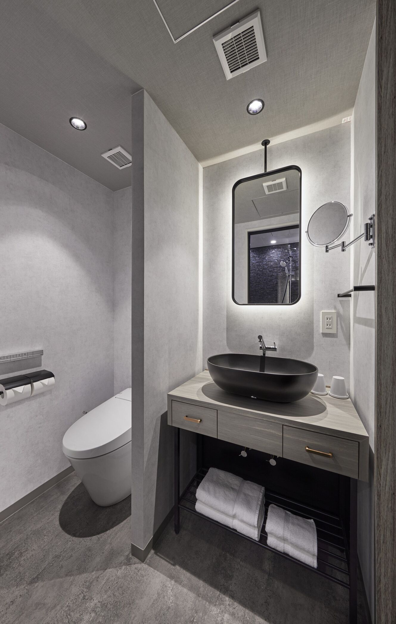Un baño moderno con un lavamanos tipo recipiente negro, un inodoro y un espejo con marco redondo.