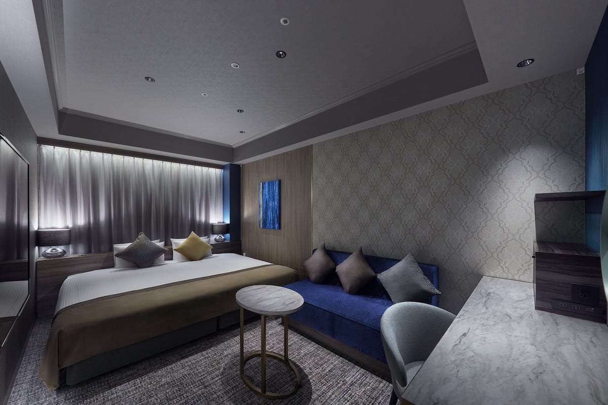 Une chambre d’hôtel moderne, dotée d’un grand lit, d’un canapé, d’une petite table ronde et d’un bureau avec une chaise.