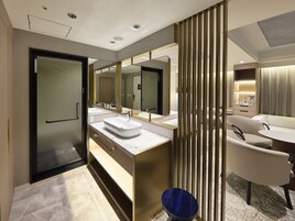 A modern bathroom with a large mirror, two sinks, and a seating area with a table and chairs.