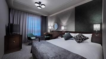 Een moderne hotelkamer met een groot bed, een bureau met stoel, een televisie en een groot raam met gordijnen.