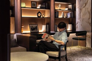 Une personne est assise dans une pièce moderne, où l’on aperçoit une bibliothèque, une lampe et une petite table.