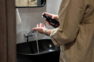 A person holding a bottle of hand soap near a sink with running water.