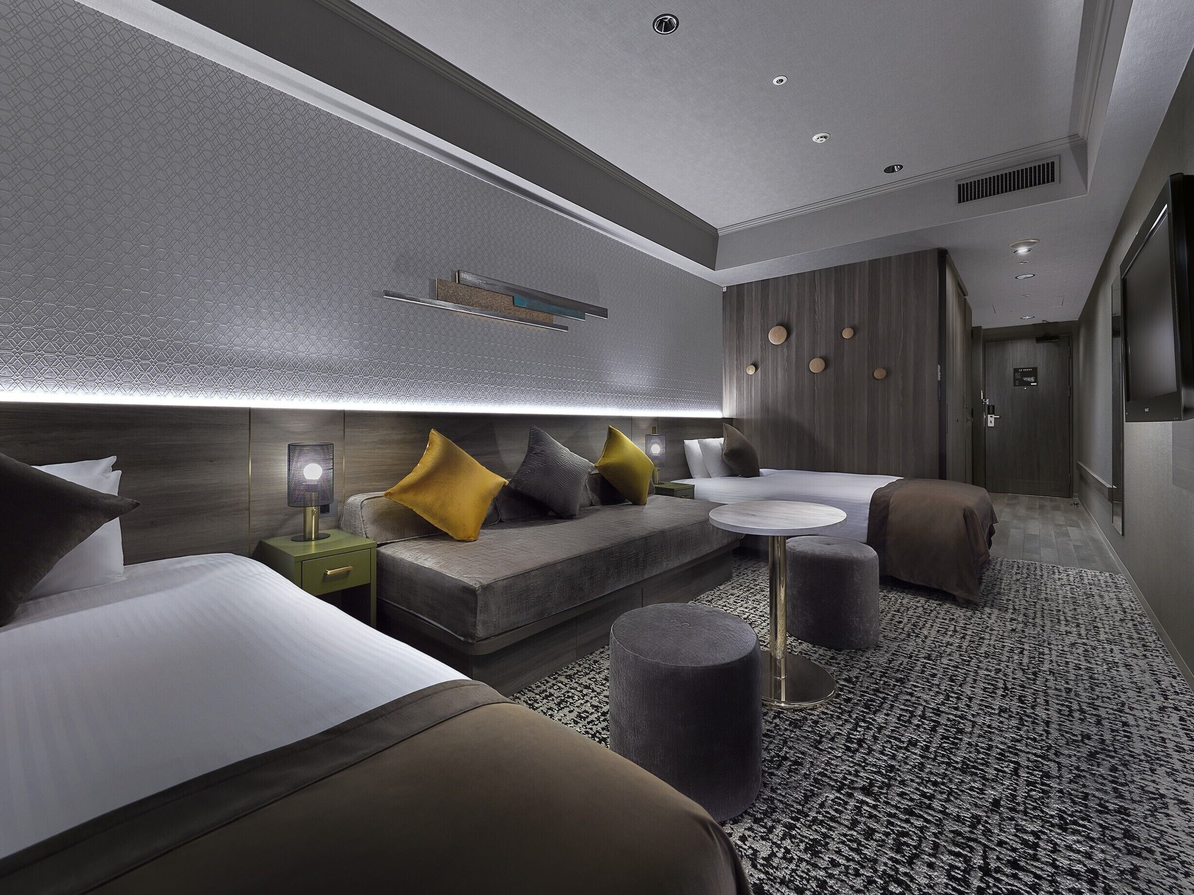 Una habitación de hotel moderna con una cama grande, un sofá, una pequeña mesa redonda y una zona de estar con una alfombra estampada.