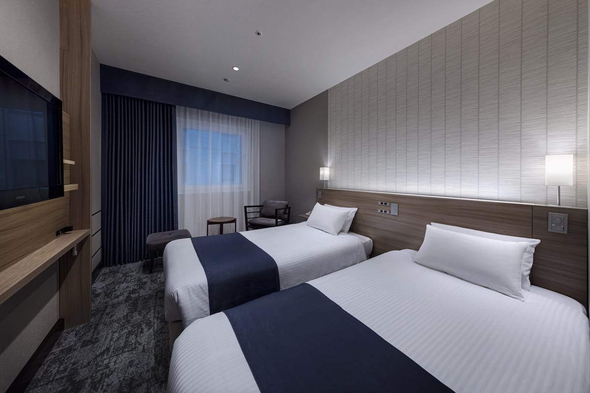 Une chambre d’hôtel avec deux lits, un bureau, une chaise et une télévision.