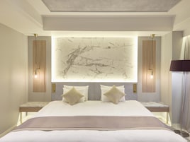 Una camera d'albergo moderna con un letto grande, una testiera in marmo e illuminazione a parete.