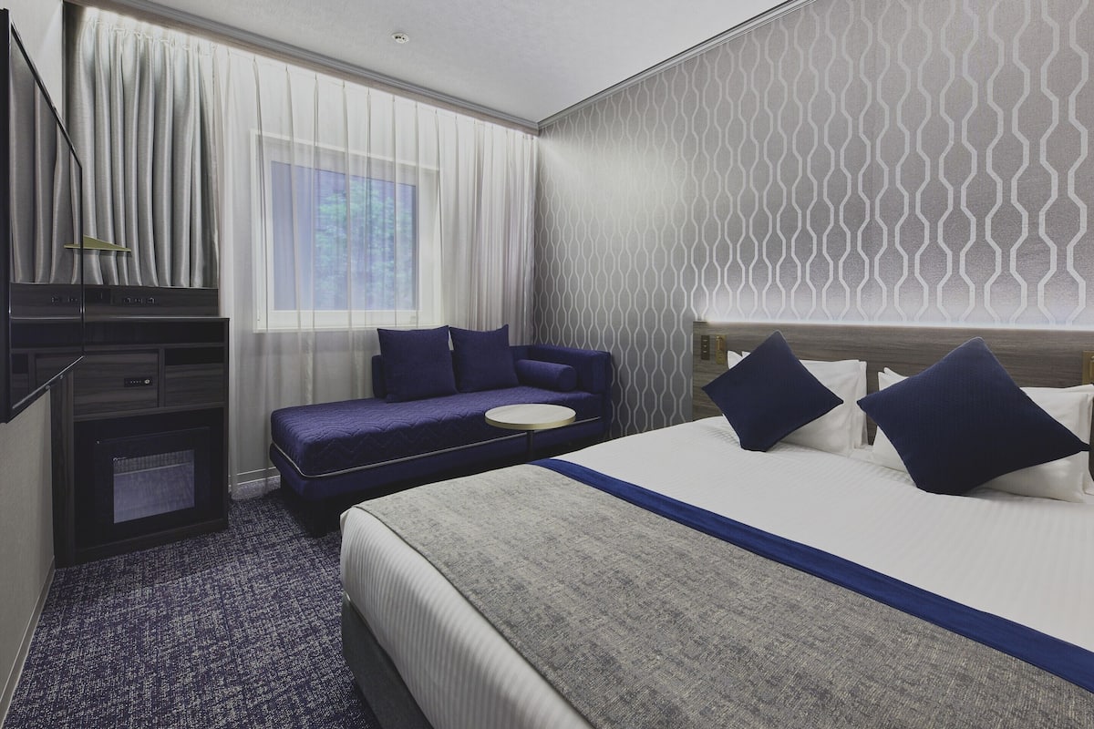 Une chambre d’hôtel avec un lit, un canapé, une télévision et une fenêtre avec des rideaux.