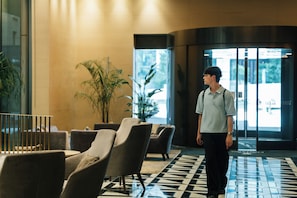 A man walking through a lobby with a checkered floor, seating area, and large windows. - Hotel Villa Fontaine Grand Tokyo - Roppongi (Tokyo)