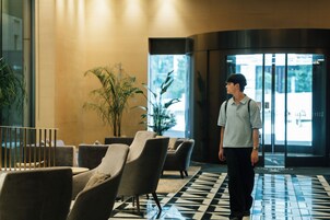 A man walking through a lobby with a checkered floor, seating area, and large windows.