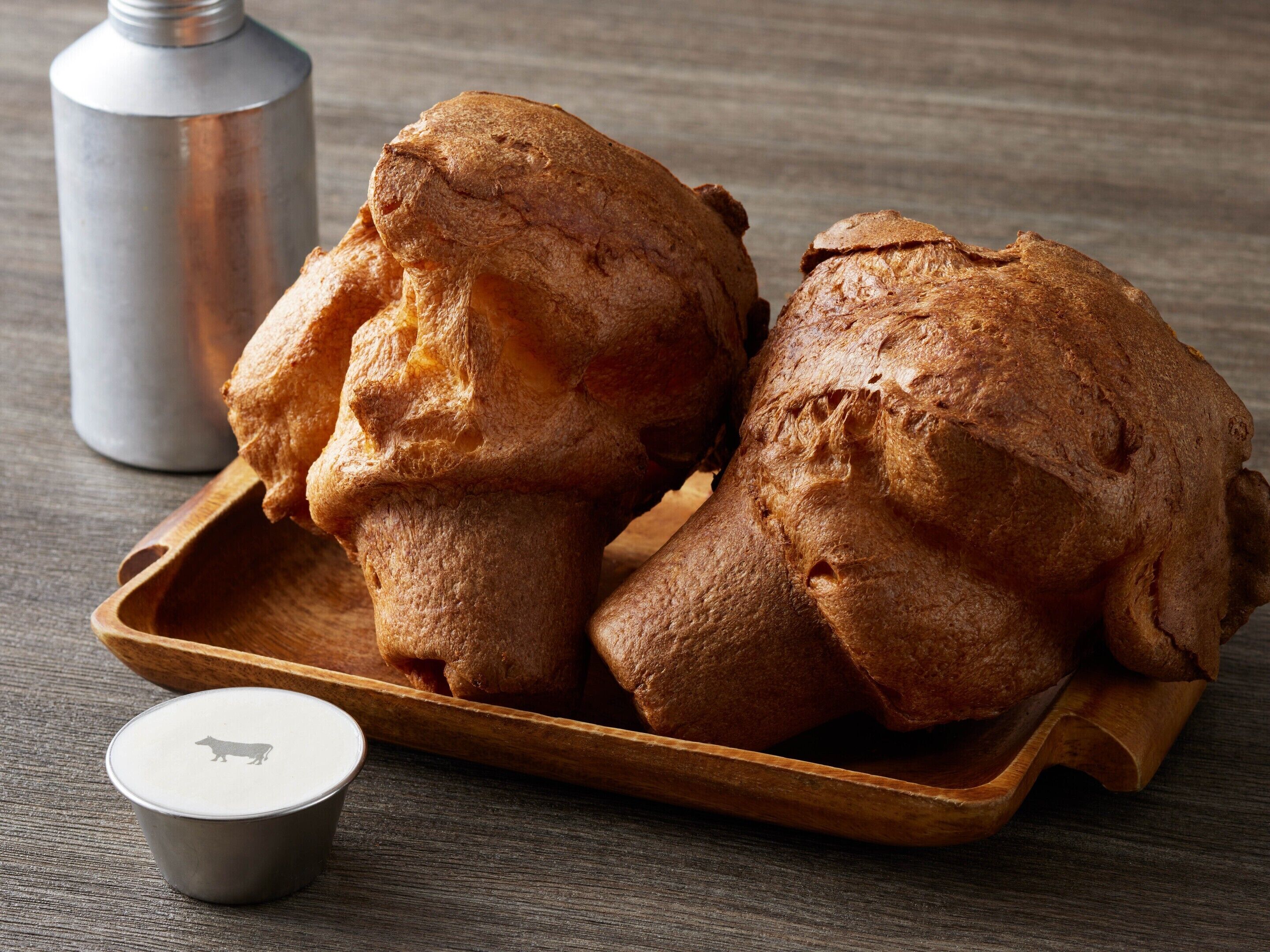 Two fried dough pastries on a wooden tray with a small cup beside them.