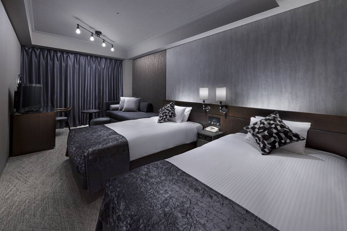 Une chambre d’hôtel moderne équipée de deux lits, d’un bureau, d’une chaise, d’une télévision et d’une grande fenêtre avec des rideaux.