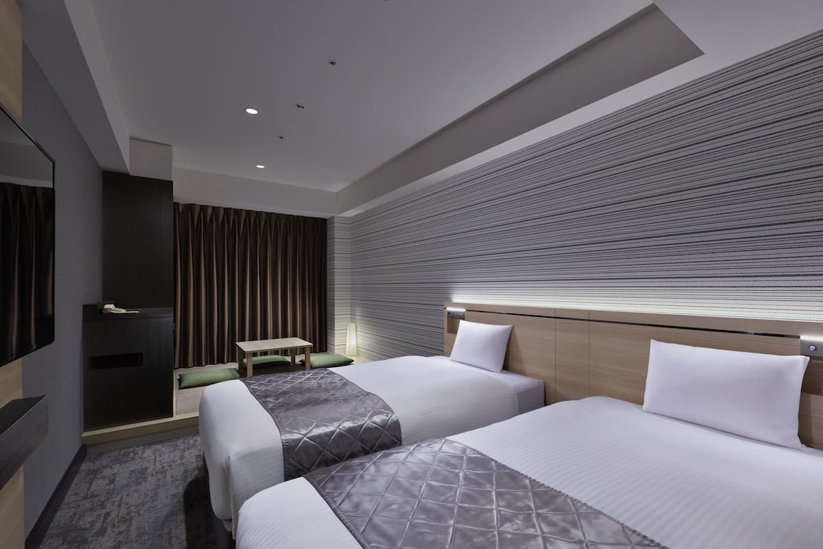 Une chambre d’hôtel moderne équipée de deux lits, d’un téléviseur à écran plat, d’un bureau et d’une grande fenêtre avec des stores.