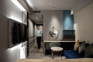 A modern hotel room with a bed, a desk, a chair, a sofa, a TV, and a mirror.