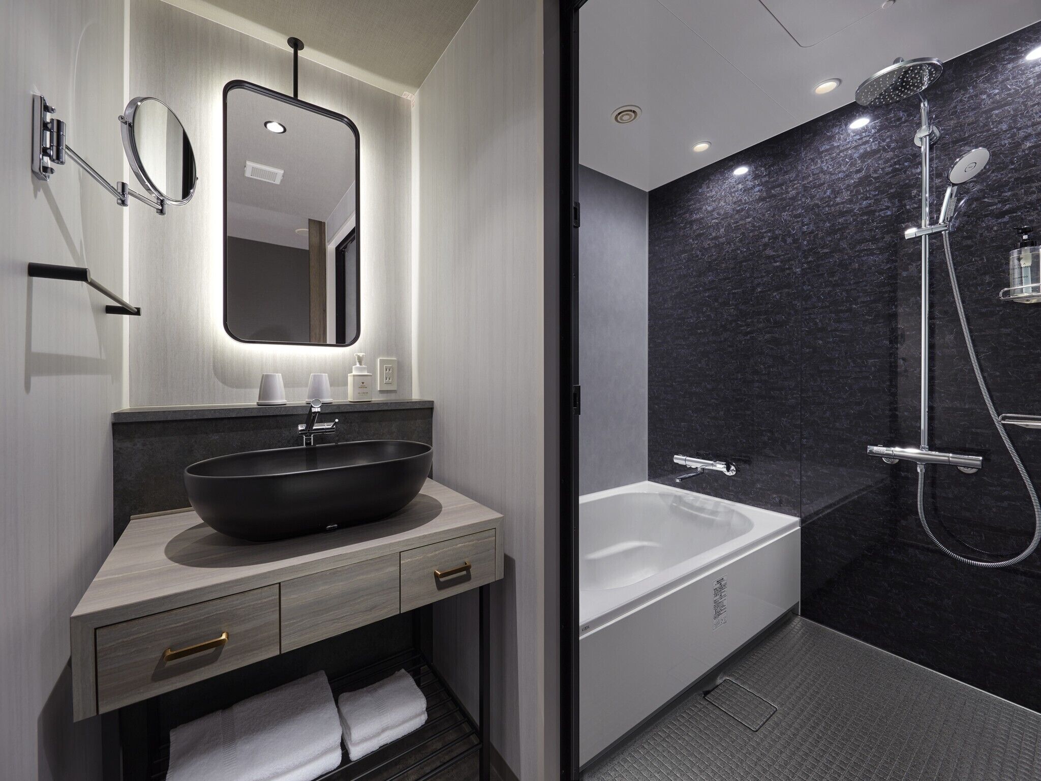 A modern bathroom with a large vessel sink, a mirror, a handheld showerhead, and a bathtub.