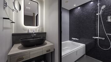 A modern bathroom with a large vessel sink, a mirror, a handheld showerhead, and a bathtub.