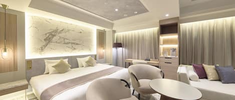 A modern hotel room with a large bed, a sofa, a desk, and a chair.