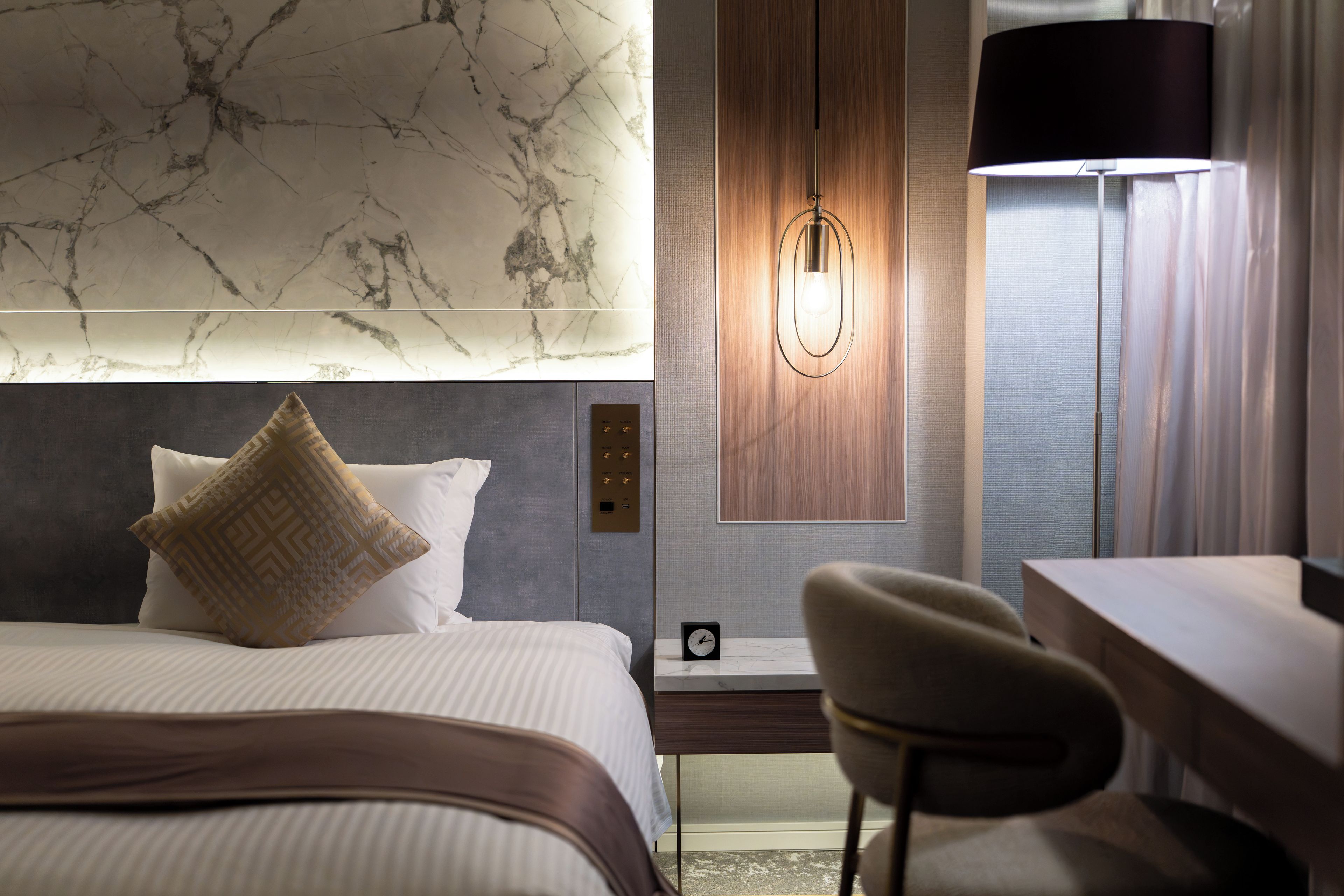 Een hotelkamer met een bed, een bureau, een stoel, een wandlamp en een klok.