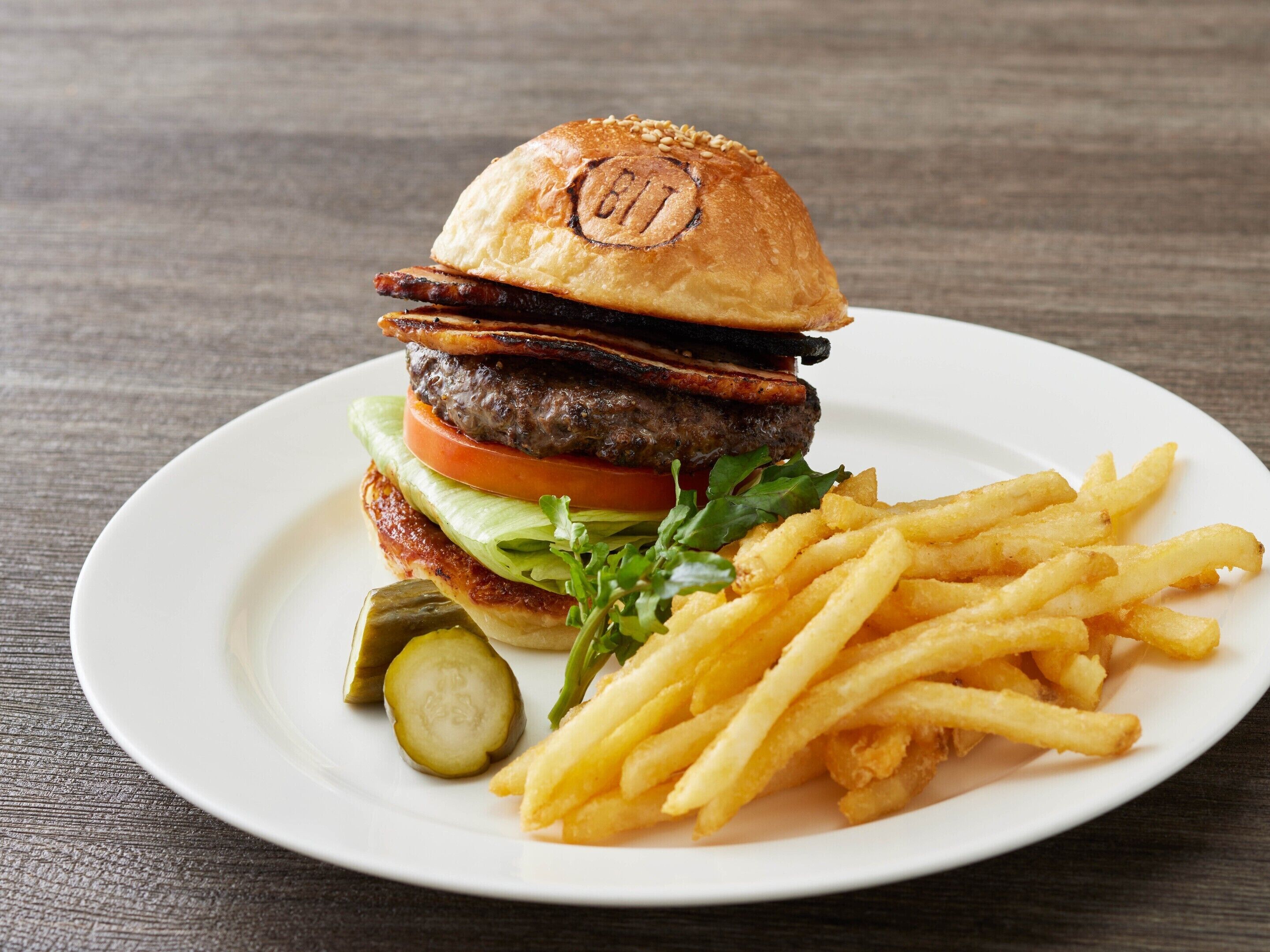 Ein Burger mit Pommes und Gurke auf einem weißen Teller.