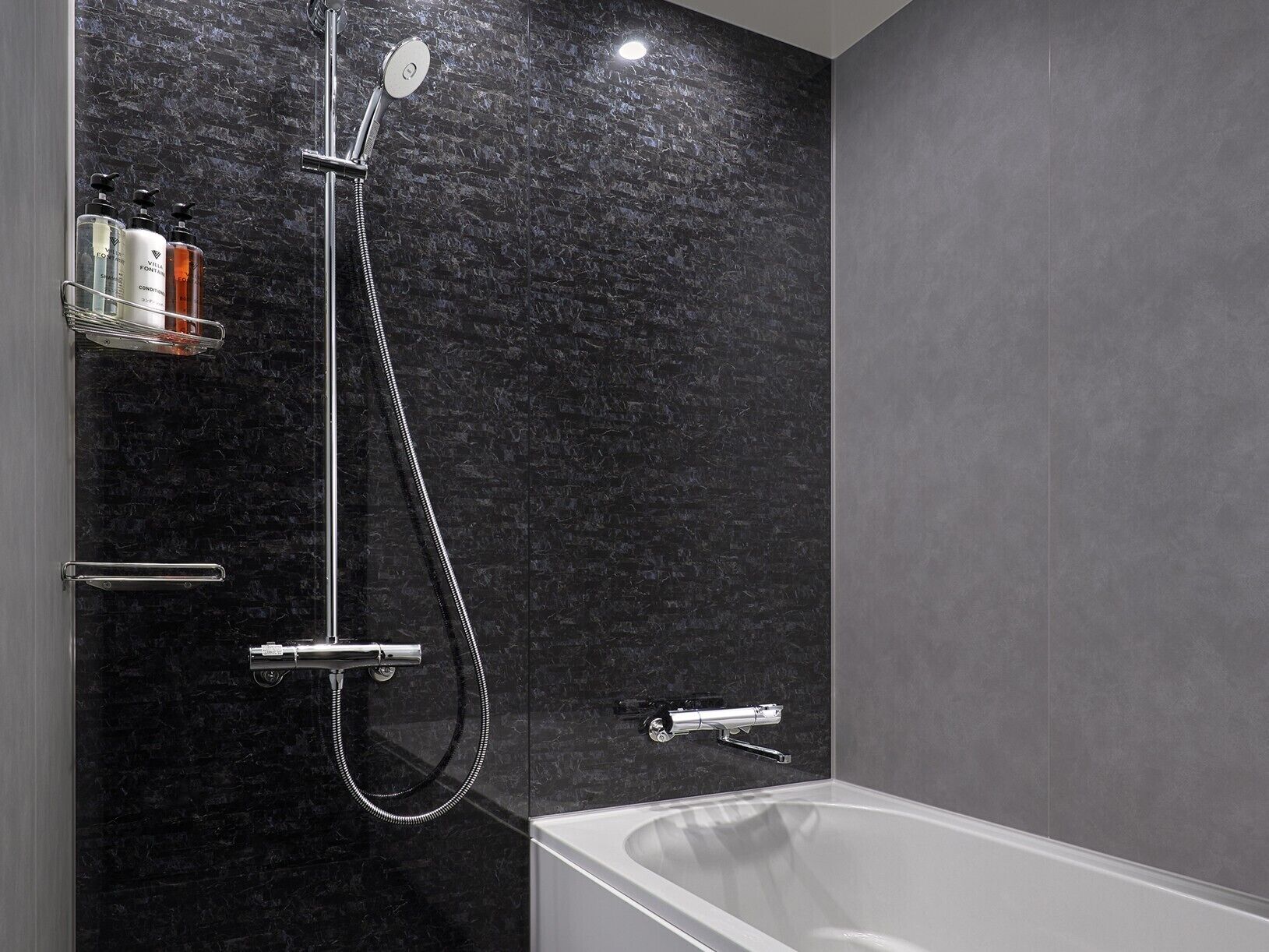 A modern bathroom with a black marble wall, a shower with a handheld showerhead, a handheld showerhead, and a bathtub.