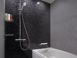 A modern bathroom with a black marble wall, a shower with a handheld showerhead, a handheld showerhead, and a bathtub.