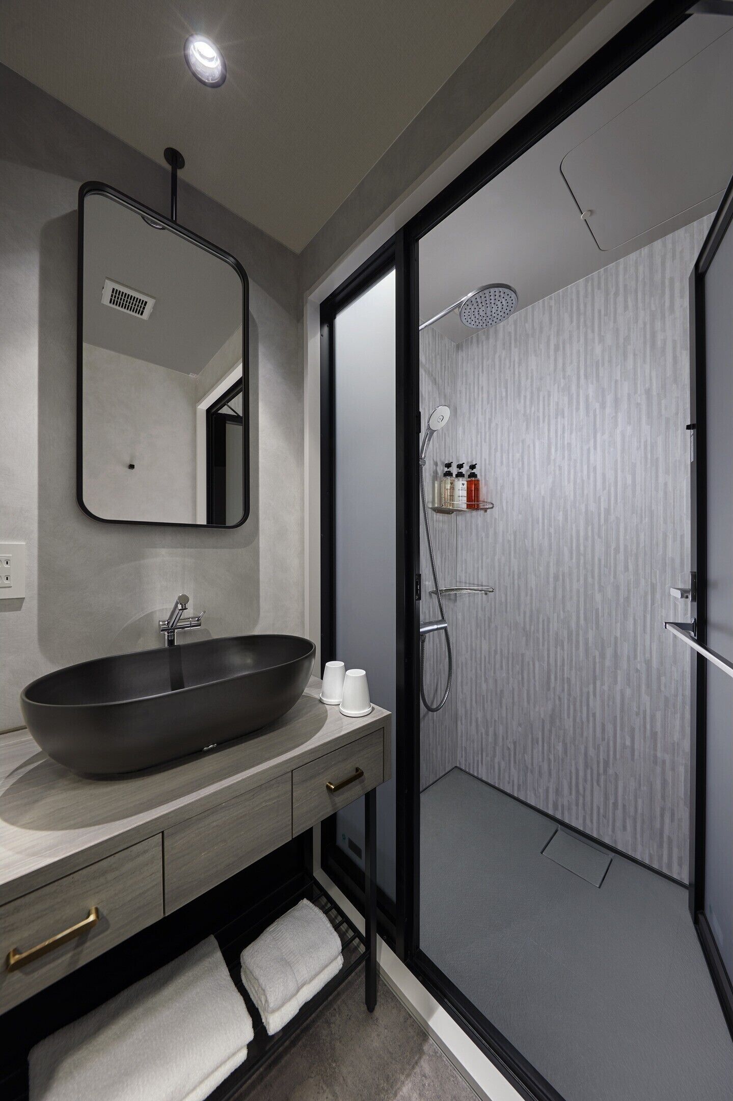 A modern bathroom with a large vessel sink, a mirror, a shower enclosure, and a towel rack.