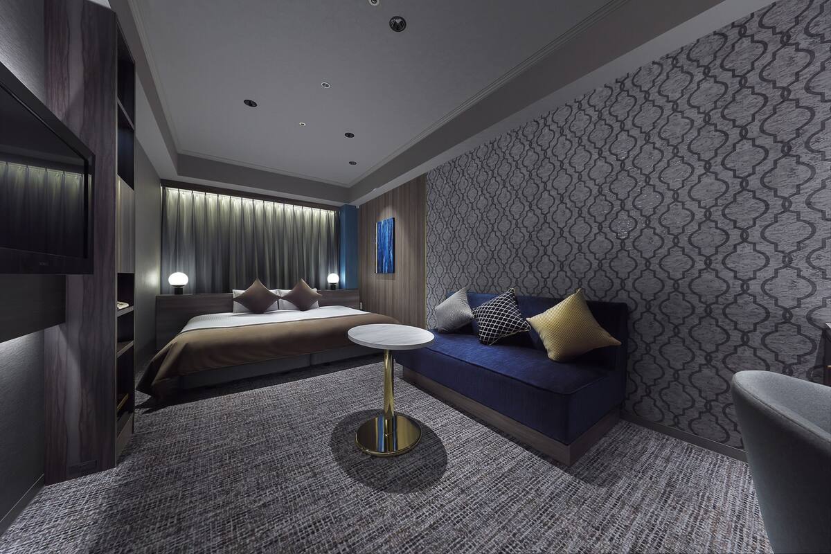 Une chambre d’hôtel moderne avec un lit, un canapé, une petite table ronde et un mur décoré de motifs.