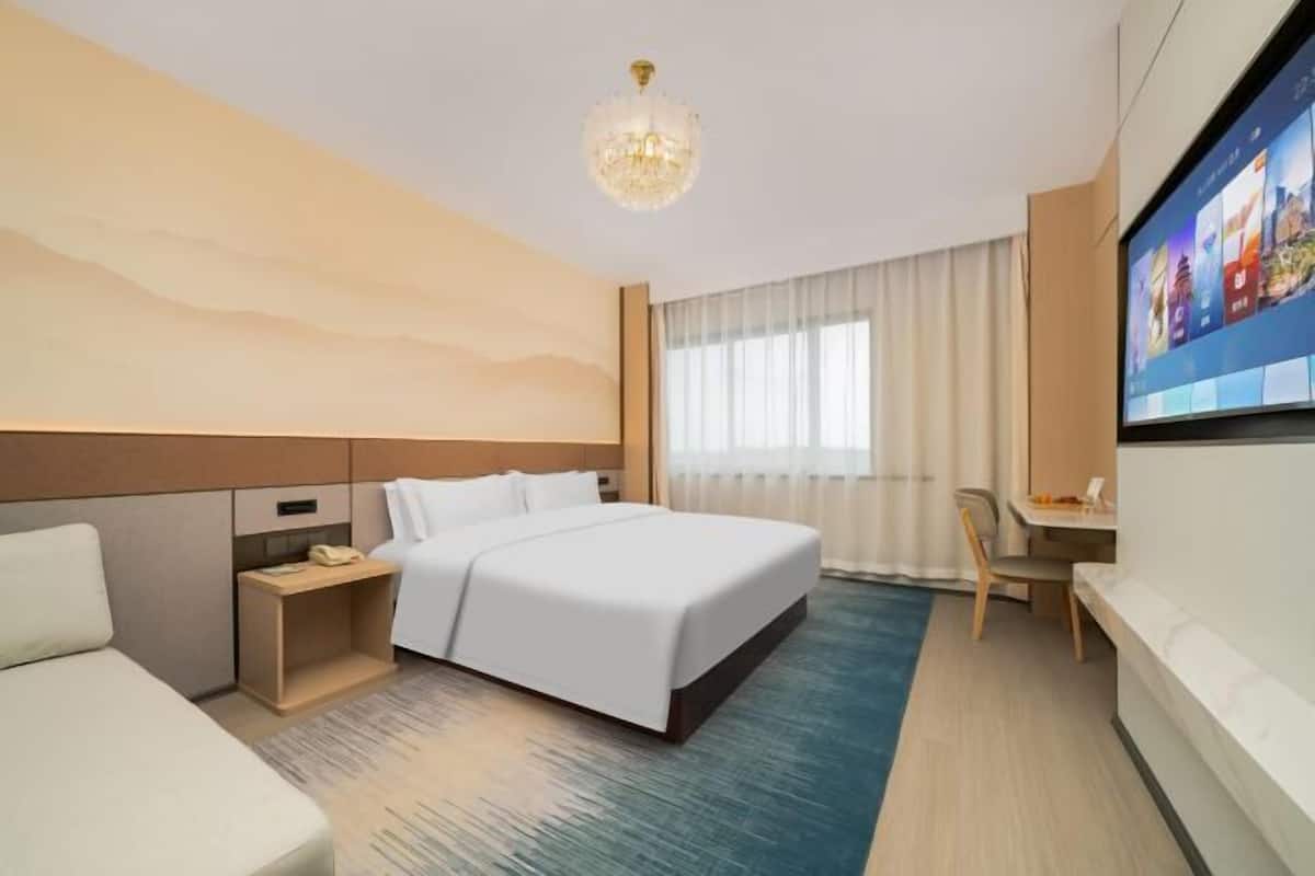 A hotel room with a bed, bedside table, desk, chair, TV, and a large window with curtains.