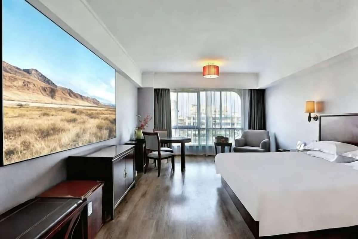 A hotel room with a large window, a bed, a desk, a chair, and a small table.
