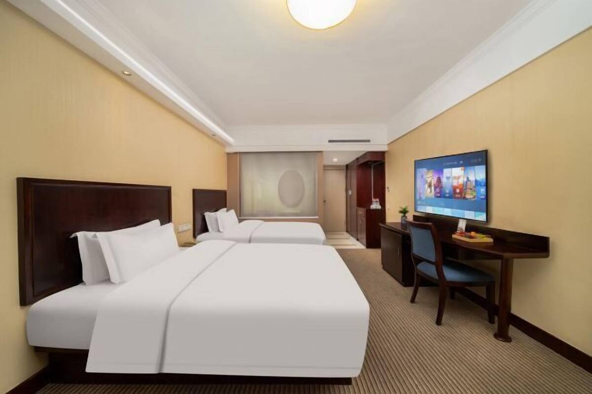 A hotel room with two beds, a desk, a television, and a large wall decoration.