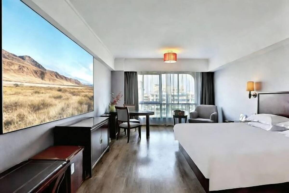 Ein Hotelzimmer mit großem Fenster, einem Bett, einem Schreibtisch, einem Stuhl und einem kleinen Tisch.
